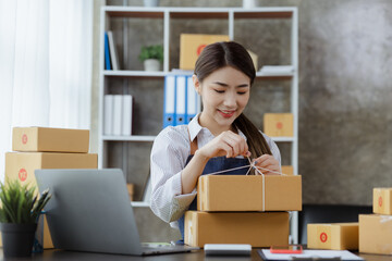 An Asian woman tying a parcel to a customer's box, she owns an online store, she packs and ships through a private transport company. Online selling and online shopping concepts.