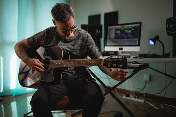 Obraz premium Guitarist and producer tuning his acoustic guitar before recording some parts for a project at his home studio