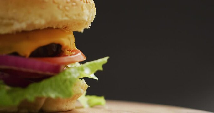 Video close up of cheeseburger with salad in burger bun, on grey background with copy space