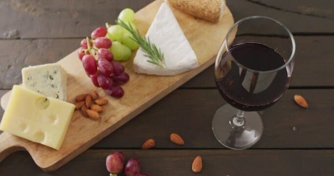 Video of cheeses, bread, grapes and nuts on board and glass of red wine on wooden table