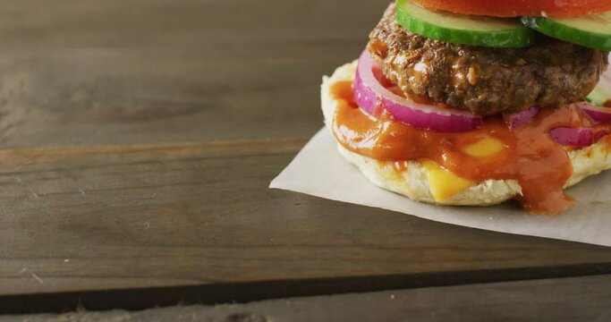 Video of hamburger with salad and relish in burger bun on wooden table top, with copy space