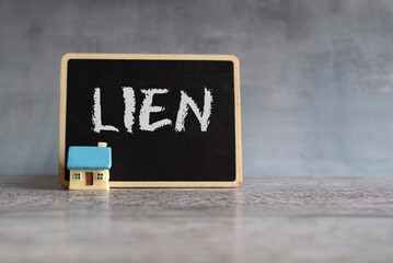 Toy house and chalkboard with text LIEN. Property and real estate concept