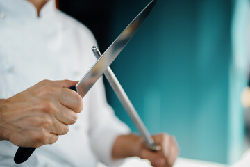 Professional restaurant kitchen, male chef sharpening a knife