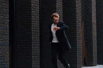 Fototapeta premium Running out of time. Stylish man with beard and in glasses is outdoors near building
