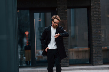 Stylish man with beard and in glasses is outdoors near building