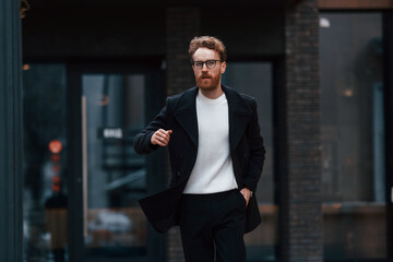 Running out of time. Stylish man with beard and in glasses is outdoors near building