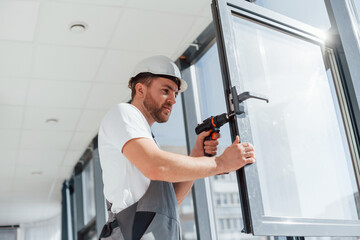 In grey uniform. Repairman is working indoors in the modern room