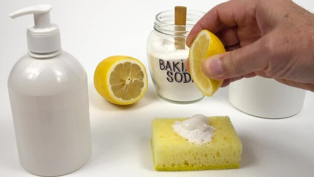 Person squeezes the juice of a lemon onto a cleaning sponge with baking soda. 