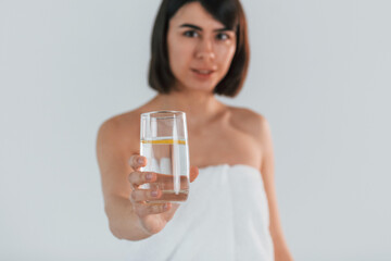 Holding glass with water. Young brunette is indoors against white background