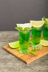 Sweet refreshing mint liqueur, with ice and mint leaves on table background, Shots with lime slice and mint flat lay