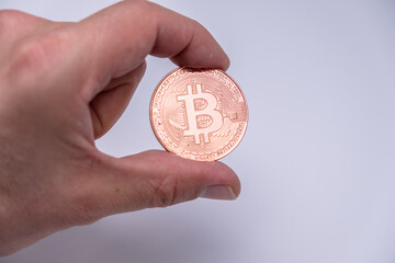 Male hand finger holding bitcoin cryptocurrency coin. close up to rose gold bit coin standing on white background. BTC most popular crypto currency money.