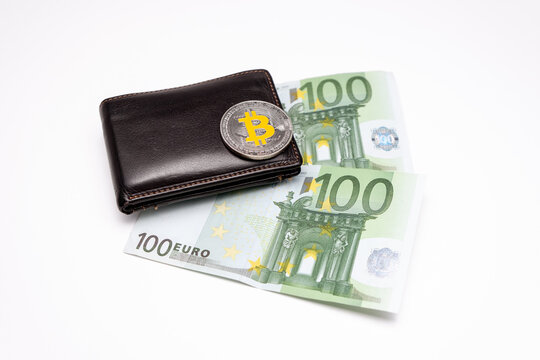 Bitcoin coin on top of wallet with  two 100 Euros banknotes on white  background. Bitcoin on wallet with two hundred euro bank notes. Cryptocurrency concept, bitcoin and Euro banknotes.