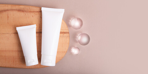 Top view of blank cosmetic tubes on wooden slice with glass spheres near.Earth tones,eco friendly concept,banner with copy space.