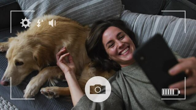 Camera interface against caucasian woman talking a selfie with her dog on the couch