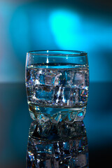 A glass with ice water and ice cubes on a blurred blue background. A refreshing and chilling drink in hot weather.