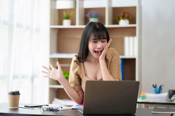 Cheerful and beautiful Asian businesswoman is very excited and delighted because she is satisfied with the work she has accomplished achieve your goals with your laptop computer.