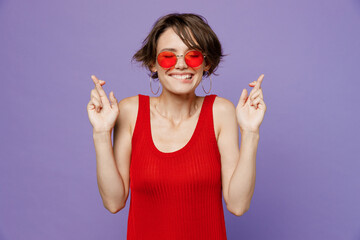 Young fun woman 20s she wear red tank shirt eyeglasses waiting for special moment, keeping fingers...