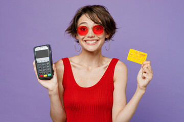 Young smiling happy woman 20s she wear red tank shirt eyeglasses hold wireless modern bank payment...