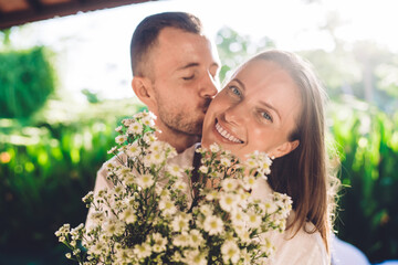 Portrait of joyful female feeling happiness and smiling at camera while receiving present of wildflowers from beloved husband, cheerful newlywed making surprises for each other on anniversary