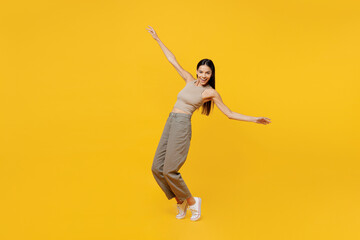Fototapeta na wymiar Full body young latin woman 30s she wear basic beige tank shirt stand on toes leaning back dance with outstretched hands isolated on plain yellow backround studio portrait. People lifestyle concept.