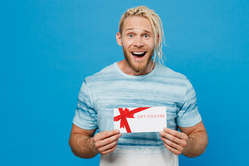 Young surprised blond man with dreadlocks 20s he wear white t-shirt hold gift certificate coupon...
