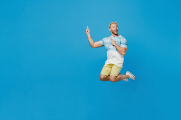Full body young blond man with dreadlocks he wear white t-shirt jump high point index finger aside on workspace area mock up copy space isolated on plain pastel light blue background studio portrait