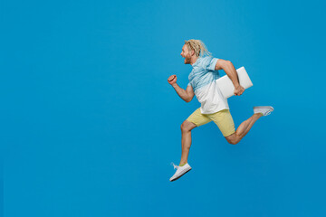 Fototapeta na wymiar Full body young blond man with dreadlocks 20s he wear white t-shirt hold closed laptop pc computer jump high run fast isolated on plain pastel light blue background studio. People lifestyle concept.