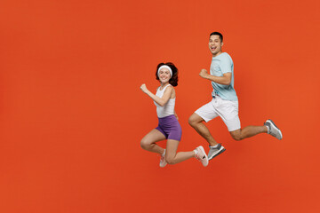 Fototapeta na wymiar Full body side view young fitness trainer instructor sporty two man woman in headband t-shirt jump high run spend weekend in gym isolated on plain orange background. Workout sport lifestyle concept.