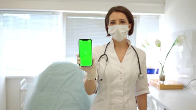 beautiful cute doctor in medical mask in medical office holds smartphone with chroma key in her hand. general practitioner. Doctor female dermatologist cosmetologist. 