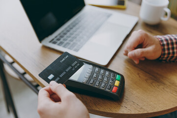 Cropped young man he wear shirt hold wireless bank payment terminal to process credit card payments sit alone at table in coffee shop cafe rest in free time. Freelance mobile office business concept