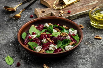 Beet or beetroot salad with baby spinach, cheese, nuts, cranberries on plate with fork, dressing and spices on gray background, top view. place for text