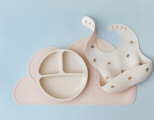 Set of silicone dishware and baby accessories on blue light background, flat lay