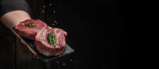Chef salts steak in a freeze motion with rosemary and spices. Preparing fresh beef or pork on a...