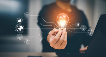 Businessman hand holding light bulb with icons and working on the desk, Creativity and innovation are keys to success.Concept of new idea and innovation with energy and power , working at home,