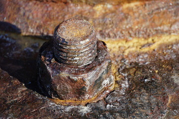 A rusty screw with a nut on a rusty metal surface