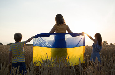 children and a woman stand with their backs against sky, setting sun, wheat field with a blue and...