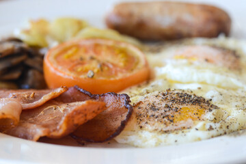 English breakfast close-up focused on the peppered fried egg and crispy bacon with the rest of the plate receding into the background