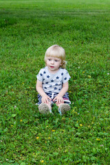 little cute blond boy sitting on the grass in the park and smiling