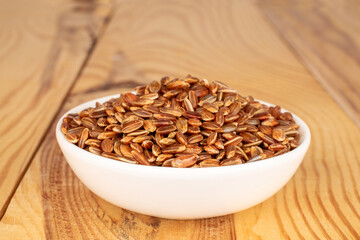 Organic uncooked brown rice in a white ceramic saucer on a wooden table, close-up.