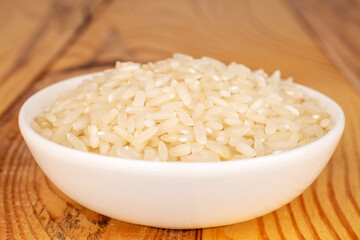 Organic uncooked rice in a white ceramic saucer on a wooden table, close-up.