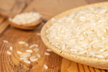Organic uncooked rice in a  ceramic saucer on a wooden table, close-up.