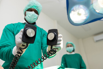 The doctor is giving a defibrillators to save the patient's life in the hospital. CPR. Using a defibrillator to save lives. Hands of man surgeon holding defibrillator at the hospital - obrazy, fototapety, plakaty