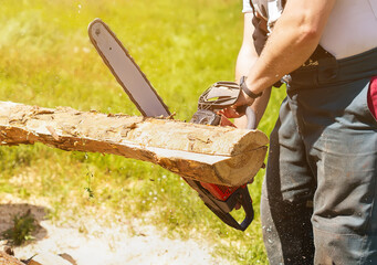 A man saws a piece of wood with a chainsaw. Working with a gasoline chain saw, close-up. The chainsaw started moving. A young man is working with a chainsaw, sawing boards for firewood in his backyard