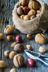 A burlap sack filled up of whole nuts with many poured out onto a rustic table.
