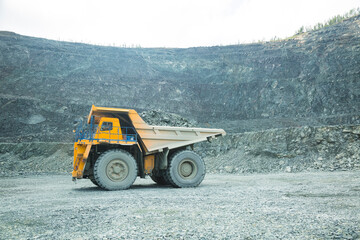 Quarry for iron ore extraction. Transportation of copper ore rocks by dump trucks. Large quarry yellow truck. Mining truck drives through the quarry, equipment for working with copper ore rocks. 