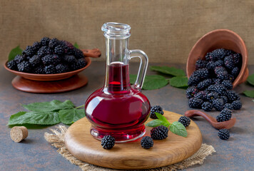 Blackberry juice or syrup in glass cruet on wooden board with fresh berries and green leaves on...