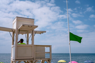Sea coast safety guard at coastal safety tower, green flag indicating safe conditions for beach visitors