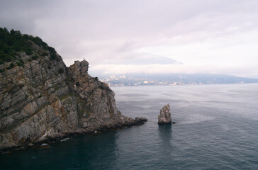 A rock in the sea with an eagle on top and a sail-shaped rock at the foot