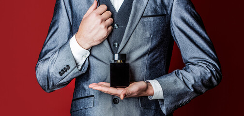 Man holding up bottle of perfume. Men perfume in the hand on suit background. Fragrance smell