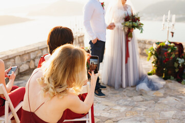 Guests at the wedding ceremony filming the bride and groom on the phones 